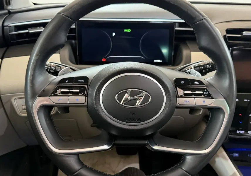 Vue rapprochée du volant cuir noir et alu du Hyundai Tucson 1.6 Hybrid 230 Executive avec tableau de bord numérique.