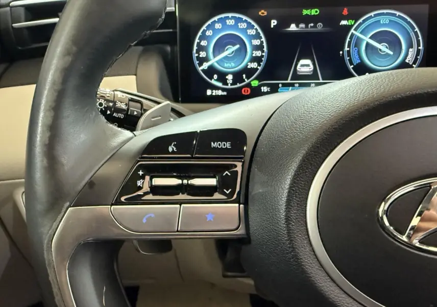 Gros plan sur le volant cuir et alu du Hyundai Tucson 1.6 Hybrid 230 Executive, avec tableau de bord digital affichant la vitesse.