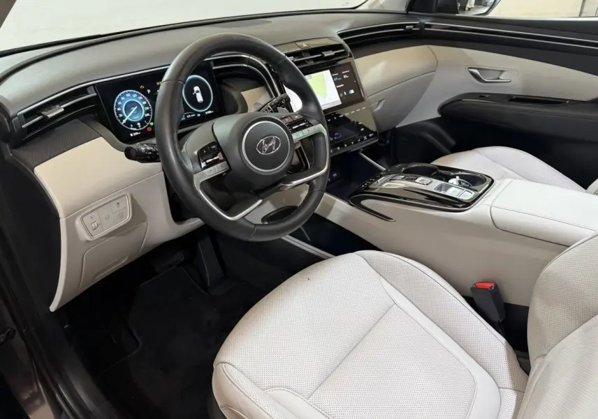 Vue intérieure côté conducteur du Hyundai Tucson 1.6 Hybrid 230 Executive avec sièges clairs et tableau de bord numérique.