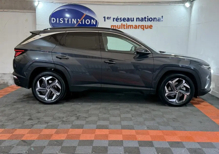 Vue de profil côté gauche d’un Hyundai Tucson gris foncé avec jantes alliage et vitres teintées en intérieur showroom.