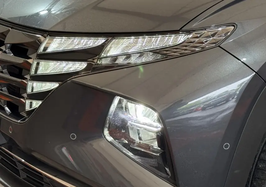 Gros plan sur l'avant droit gris foncé du Hyundai Tucson 1.6 Hybrid 230 Executive, mettant en valeur les phares LED et la calandre.