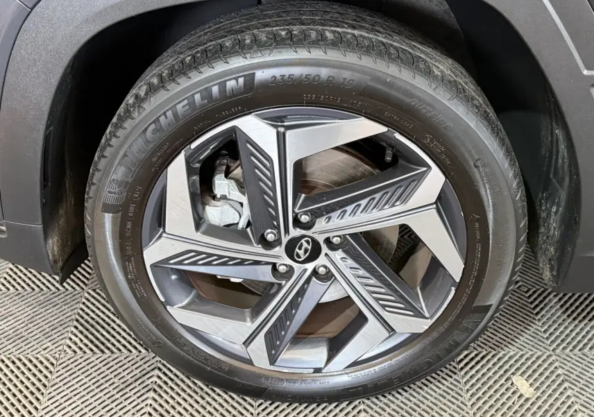Gros plan sur la roue avant droite du Hyundai Tucson gris foncé, avec jante alliage au design géométrique moderne.
