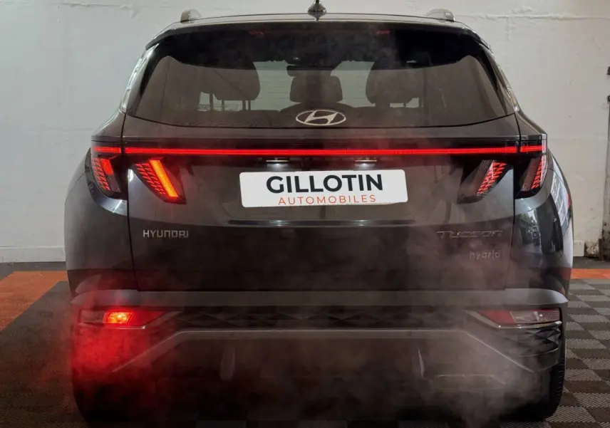 Vue arrière d'un Hyundai Tucson gris foncé avec feux arrière LED allumés et logo visible sur le hayon.