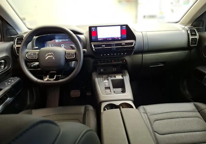 Vue intérieure avant du Citroën C5 Aircross 2025, tableau de bord et volant noir avec écran tactile central lumineux.