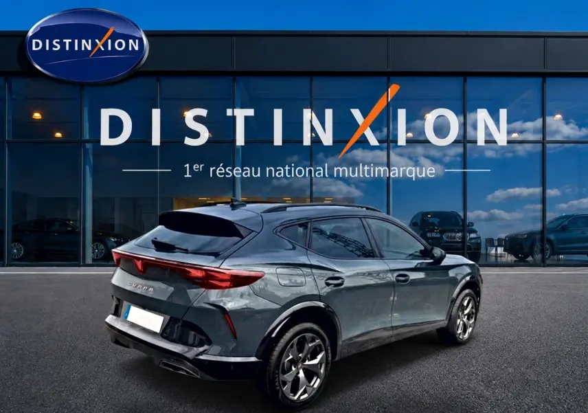 Vue 3/4 arrière droite d'une CUPRA Formentor bleu fjord avec feux arrière LED et jantes 18 pouces devant un showroom Distinxion.