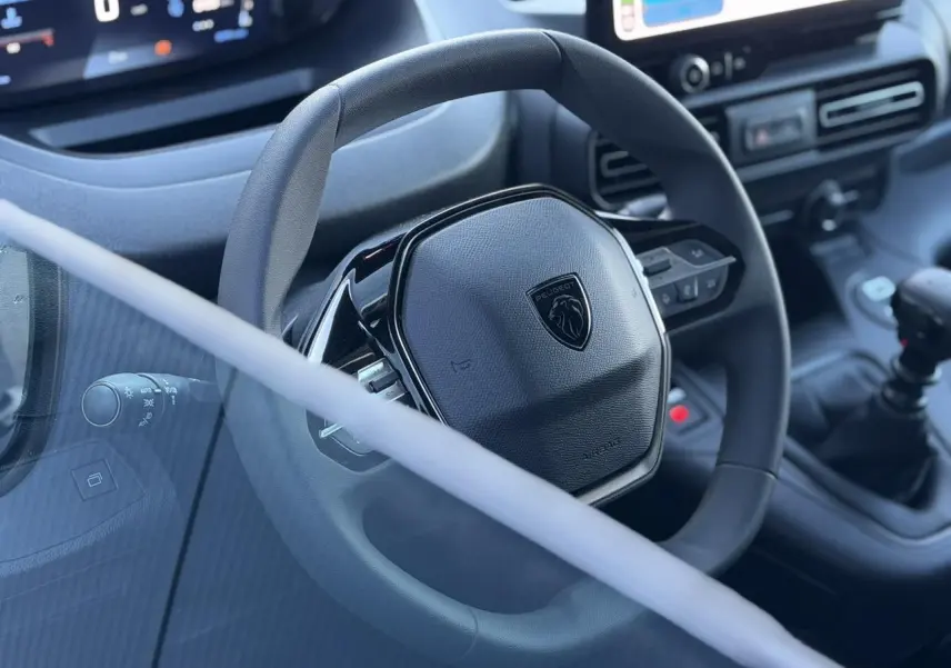Vue rapprochée du volant Peugeot noir mat avec logo lion et tableau de bord numérique du Partner 2026.