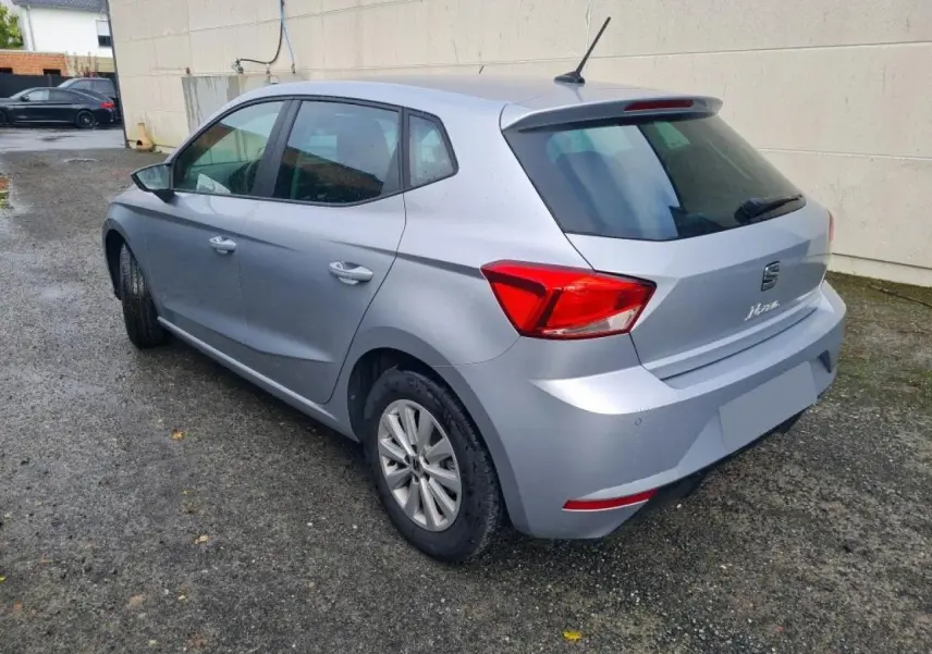 Vue 3/4 arrière droite d'une SEAT Ibiza argent urbain garée près d'un mur, avec feux arrière rouges visibles.