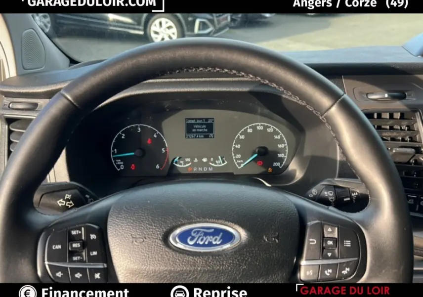 Vue intérieure centrée sur le volant en cuir noir avec logo Ford et tableau de bord du Transit Custom 2023.