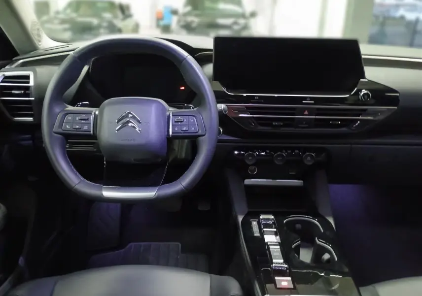 Vue intérieure avant du Citroën C5 X 2024 avec tableau de bord noir, volant cuir et écran tactile central large.