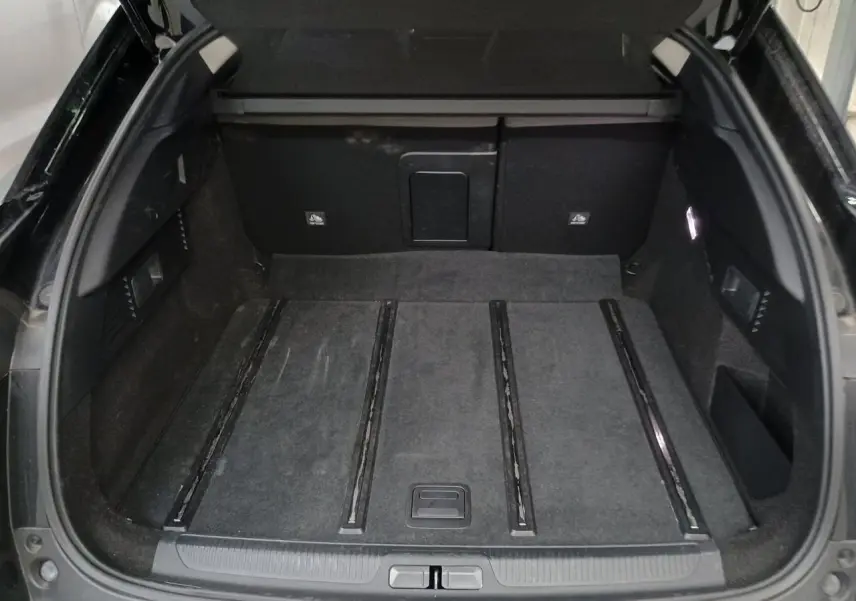 Coffre ouvert vu de l'arrière d'une Citroën C5 X Noir Perla, avec tapis de sol et rangements latéraux visibles.