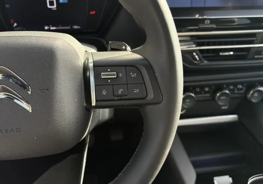 Gros plan sur le volant cuir noir du Citroën C5 X 2024 avec commandes audio et tableau de bord numérique en arrière-plan.