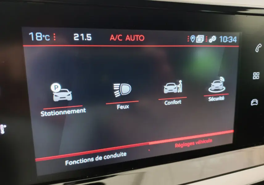 Écran tactile intérieur de la Peugeot 208 blanc, affichant les réglages de stationnement, feux, confort et sécurité.