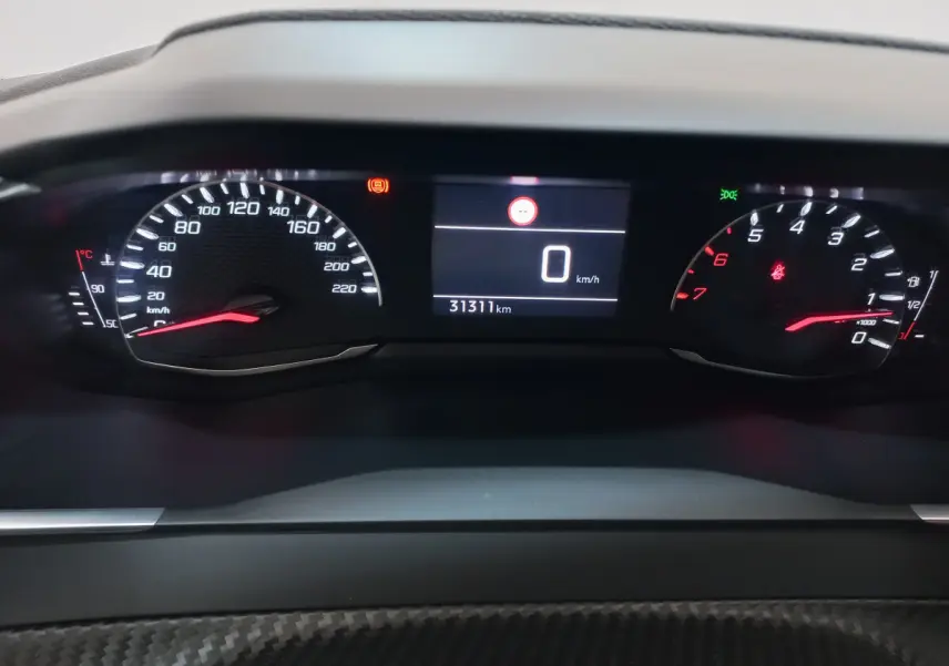 Tableau de bord numérique de Peugeot 208 PureTech 100, affichage vitesse et compte-tours avec éclairage rouge et blanc.
