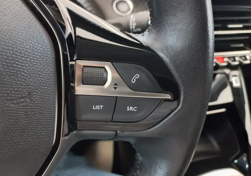 Gros plan sur les commandes noires du volant cuir du Peugeot 208 PureTech 100 S&S Allure 2021, intérieur moderne.