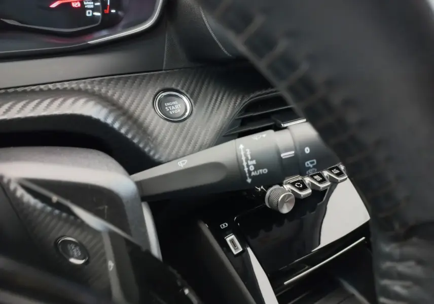 Gros plan intérieur sur le bouton démarrage et commandes du volant cuir, avec habillage carbone du tableau de bord.