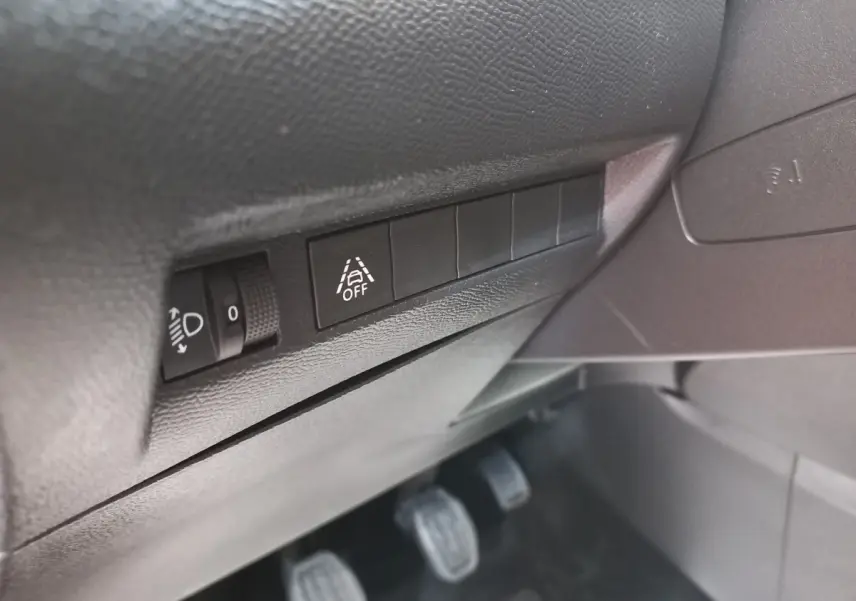 Gros plan sur les commandes de réglage des phares et désactivation de l’assistance au maintien de voie dans une Peugeot 208 blanche.
