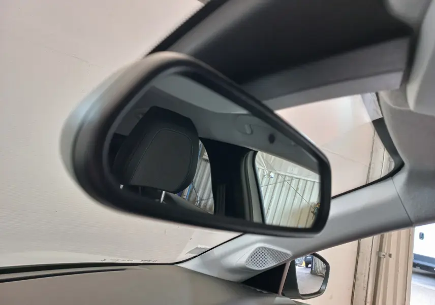 Vue intérieure du rétroviseur gauche d'une Peugeot 208 blanche 2021, avec appui-tête et partie du tableau de bord visibles.