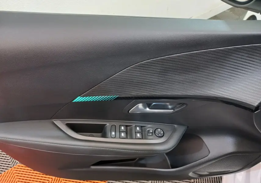 Vue intérieure du panneau de porte côté conducteur de la Peugeot 208 blanc, avec commandes électriques et insert décoratif noir à motif carbone.