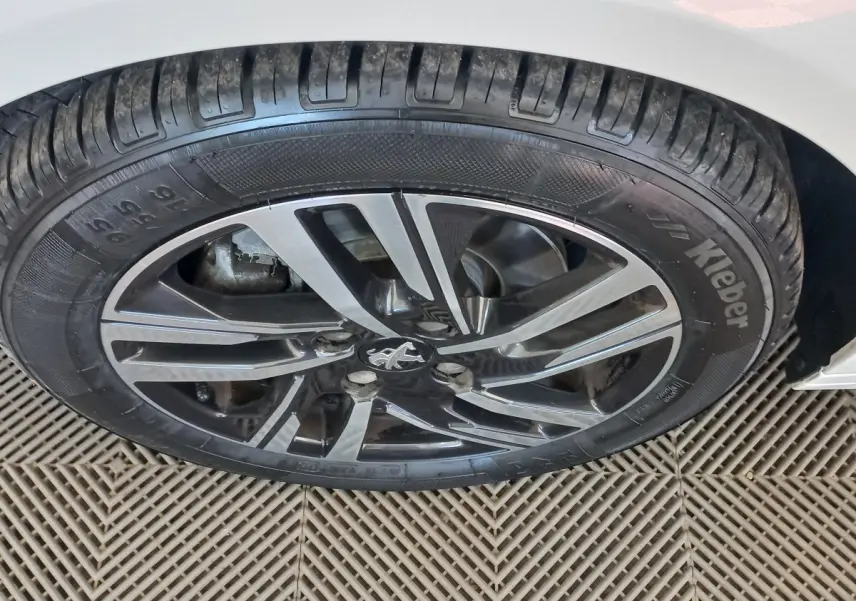 Gros plan sur la roue avant droite d'une Peugeot 208 blanche, avec jante alliage noire et argentée.