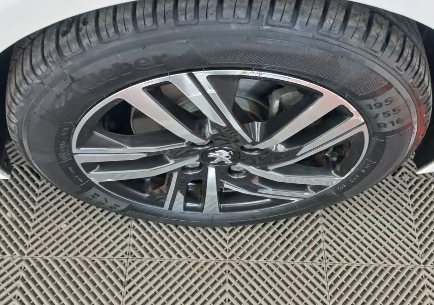 Gros plan sur la roue avant droite de la Peugeot 208 blanche, mettant en valeur la jante alliage bicolore et le pneu Kleber.