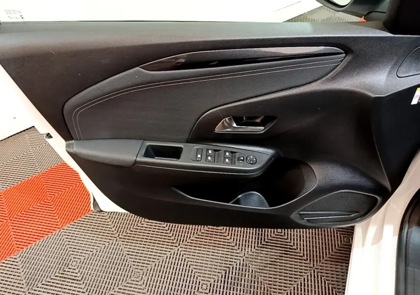 Vue rapprochée de la porte avant gauche noire d'une Opel Corsa blanche, avec commandes électriques et haut-parleur intégré.
