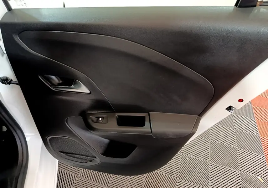 Vue rapprochée de la porte arrière gauche noire d'une Opel Corsa blanche, avec poignée et haut-parleur intégrés.