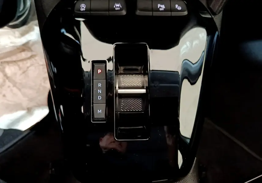 Gros plan sur la console centrale noire brillante de l’Opel Corsa 1.2 Turbo, avec sélecteur de boîte automatique et boutons de contrôle.