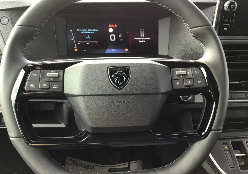 Vue rapprochée du volant noir du Peugeot Expert XL avec commandes intégrées et tableau de bord digital affichant des alertes.