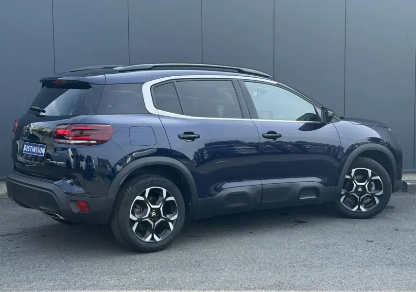 Vue 3/4 arrière droite d'un Citroën C5 Aircross Bleu Eclipse avec jantes alliage bi-ton et barres de toit noires.
