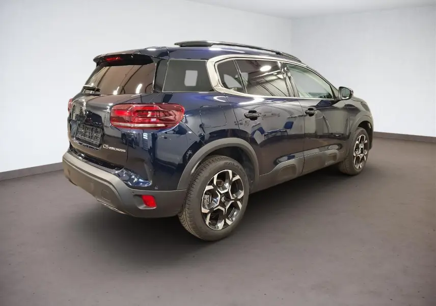 Vue 3/4 arrière droit d'un Citroën C5 Aircross Bleu Eclipse avec jantes alliage bi-ton et barres de toit noires.