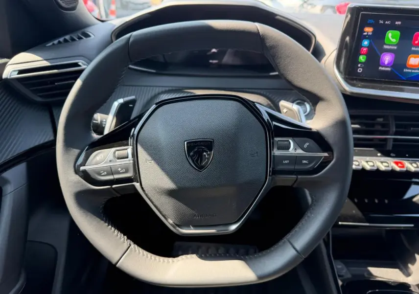 Vue rapprochée du volant noir du Peugeot 2008 Hybrid 145 e-DCS6 Allure 2025 avec tableau de bord et écran tactile visible.