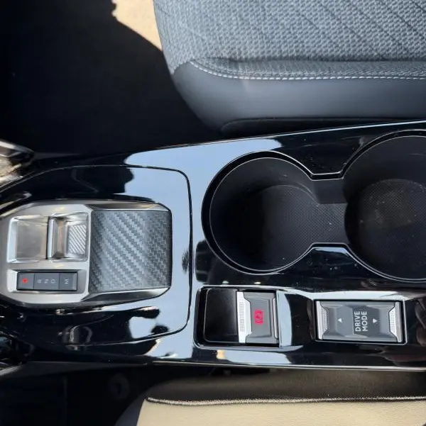 Vue rapprochée de la console centrale noire brillante du Peugeot 2008 Hybrid 145 Allure avec boutons Drive Mode et frein à main électronique.