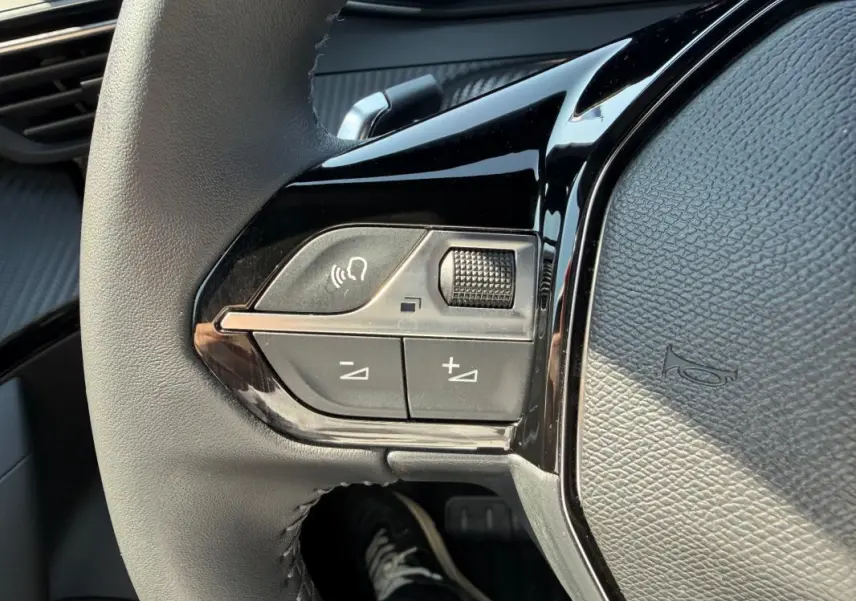 Gros plan sur les commandes gauche du volant gris du Peugeot 2008 Hybrid 145 e-DCS6 Allure 2025, avec boutons de volume et appel.