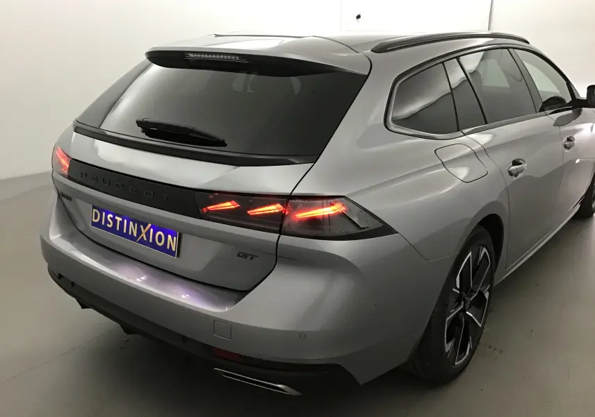 Vue 3/4 arrière droite d'une Peugeot 508 SW GT gris Artense avec feux arrière LED allumés dans un studio blanc.