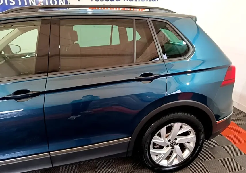 Vue latérale côté droit du Volkswagen Tiguan bleu hybride rechargeable, mettant en valeur la roue arrière et les vitres teintées.