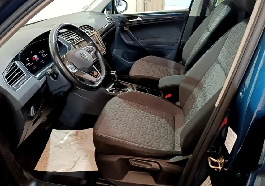 Intérieur du Volkswagen Tiguan bleu 2021, vue côté conducteur, volant cuir et sièges tissu gris à motifs géométriques.