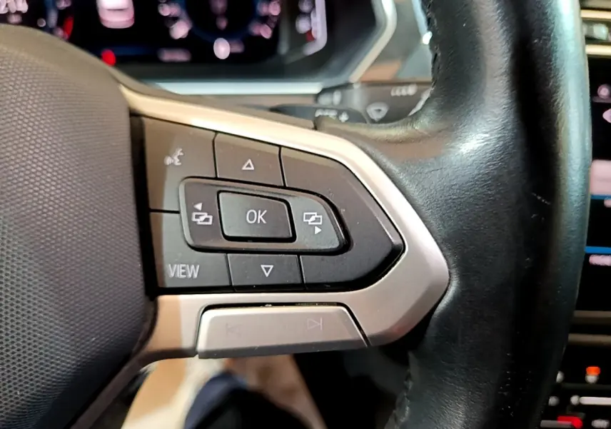 Gros plan sur les commandes multifonctions noires et argent du volant cuir du Volkswagen Tiguan bleu hybride rechargeable.