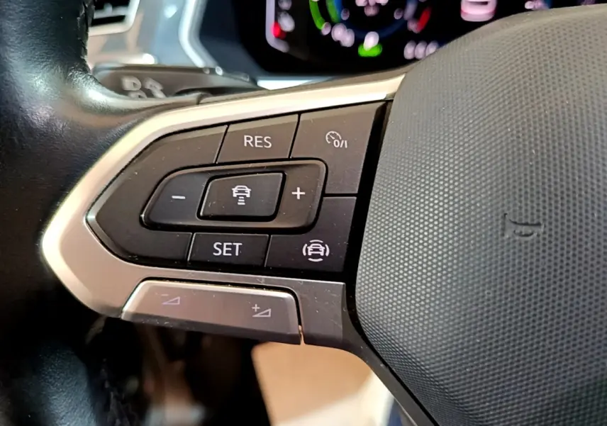 Gros plan sur les commandes de régulateur de vitesse au volant cuir du Volkswagen Tiguan bleu hybride rechargeable.