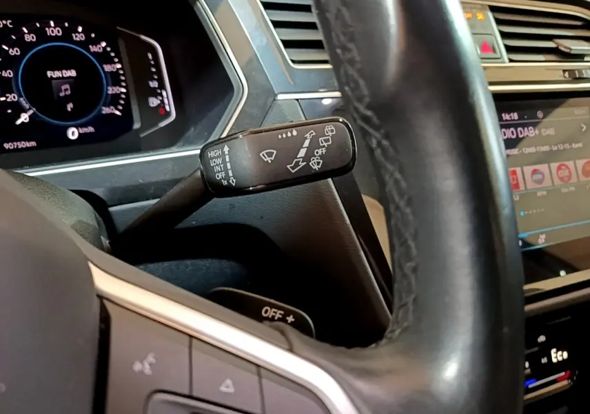 Gros plan sur le volant cuir noir et le commodo d’essuie-glace du Volkswagen Tiguan 1.4 eHybrid bleu, tableau de bord digital visible.