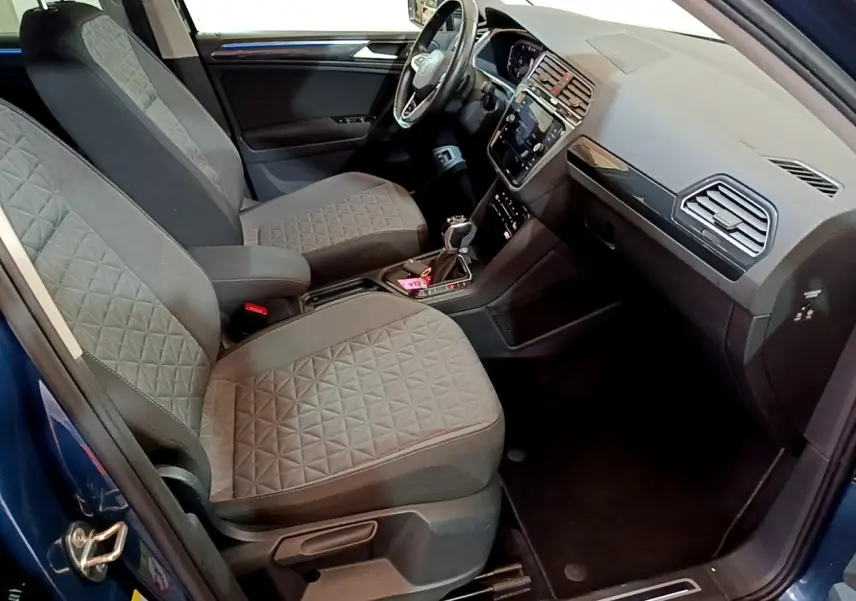 Vue intérieure côté conducteur du Volkswagen Tiguan bleu, montrant sièges tissu gris et tableau de bord moderne avec écran tactile.