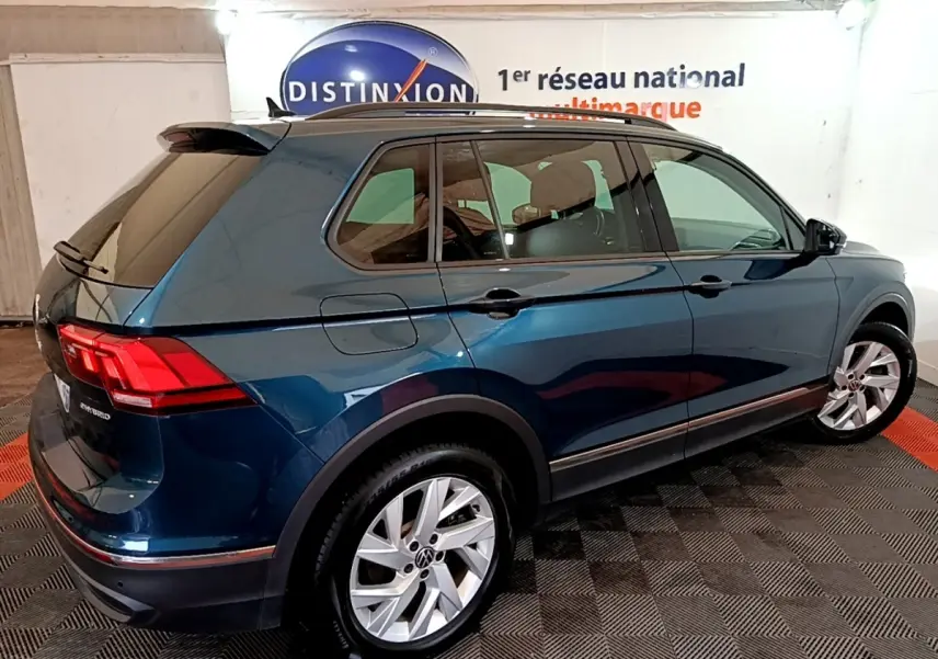 Vue 3/4 arrière droite d'un Volkswagen Tiguan bleu hybride rechargeable avec jantes alliage et vitres teintées.
