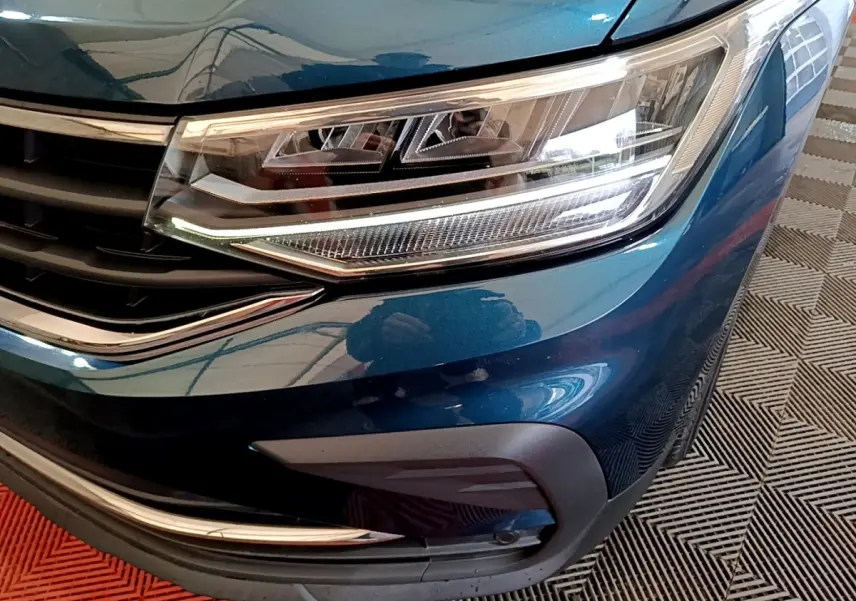 Gros plan sur le phare avant droit bleu métallisé du Volkswagen Tiguan 1.4 eHybrid avec calandre chromée.