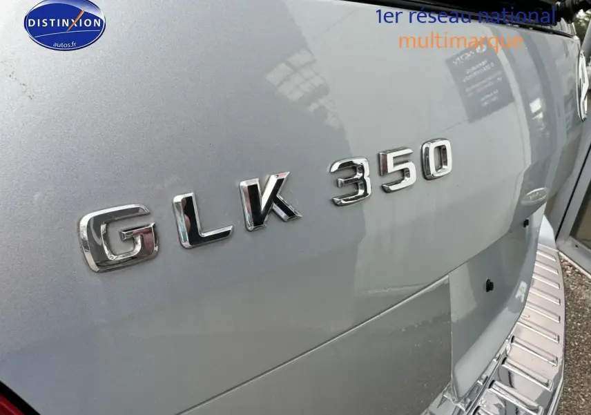 Gros plan sur le logo GLK 350 en chrome sur la porte arrière d’un Mercedes noir, avec marchepied visible.