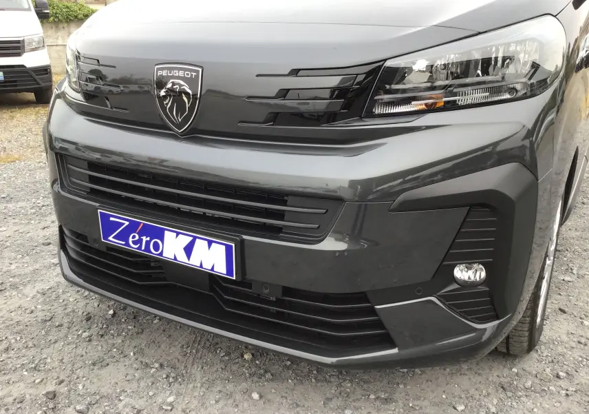 Vue de face rapprochée du Peugeot Expert cabine approfondie gris titane avec logo lion et calandre noire brillante.