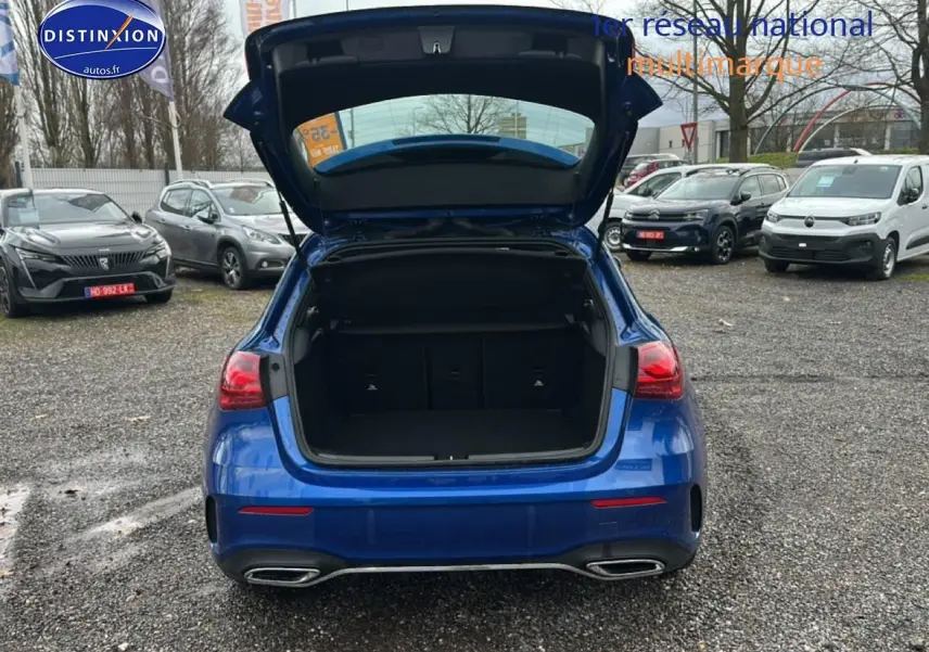 Vue arrière d'une Mercedes Classe A 180 AMG Line bleu avec coffre ouvert sur parking extérieur.