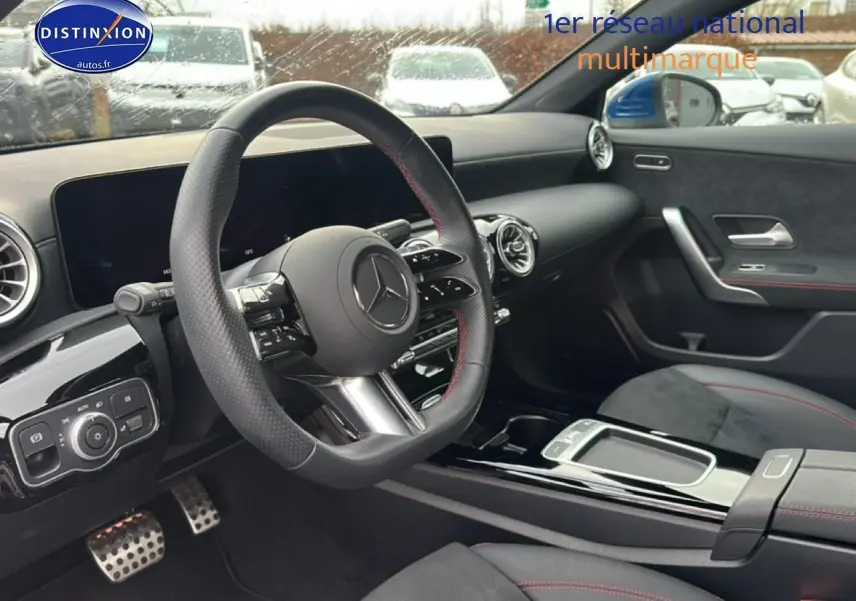 Intérieur noir avec volant sport cuir, tableau de bord numérique et surpiqûres rouges visibles côté conducteur.