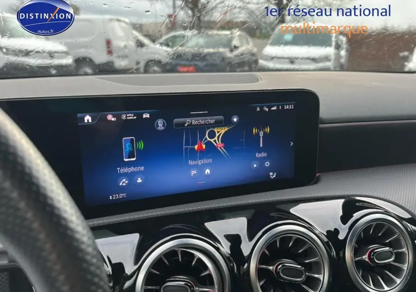 Vue intérieure centrée sur l'écran tactile et les aérateurs ronds du tableau de bord d'une Mercedes Classe A 180 AMG Line bleu.