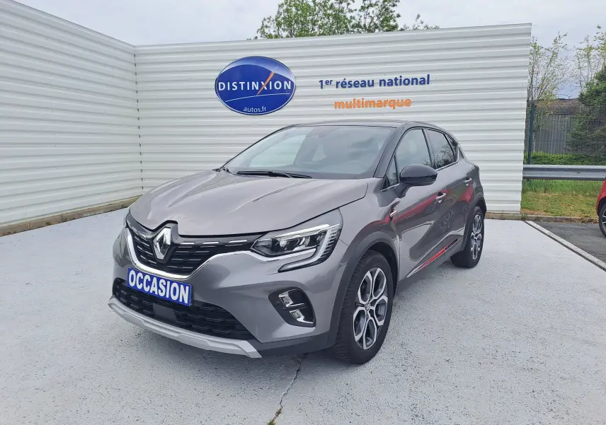 Renault Captur gris Cassiopée avec toit noir, vue 3/4 avant droit, sur parking devant un mur blanc.