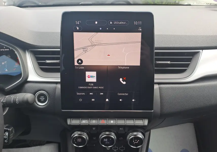 Vue intérieure centrée sur l'écran tactile du tableau de bord du Renault Captur gris Cassiopée avec toit noir, affichant la navigation et la radio.