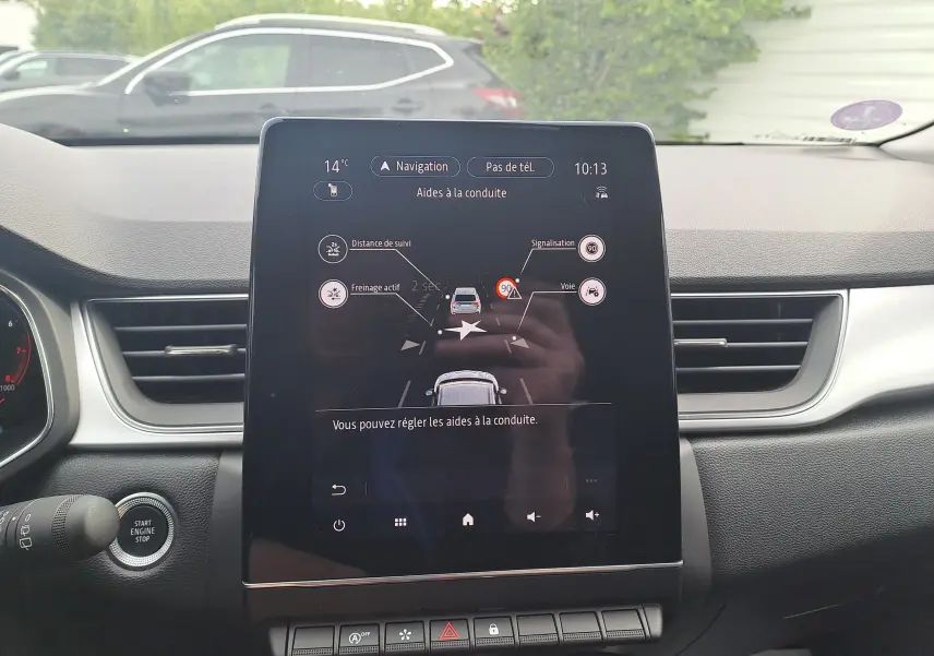 Vue intérieure centrée sur l’écran tactile du tableau de bord du Renault Captur gris cassiopée avec toit noir, affichant les aides à la conduite.